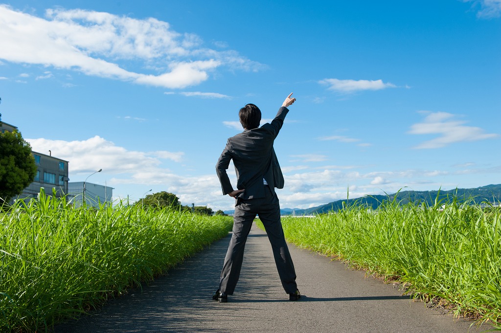 腰に手をあてて上を指さすビジネスマンの後ろ姿